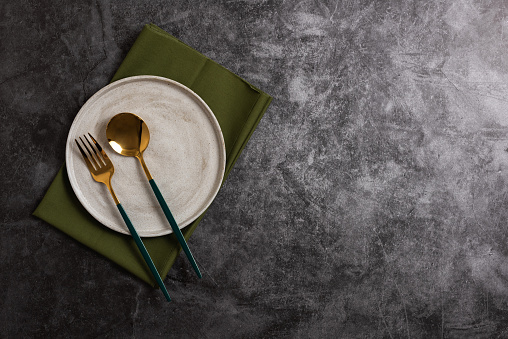 Trendy minimal tableware setting with the gray plate and golden cutlery on concrete background. Copy space for text, top view. Scandinavian-style plate template