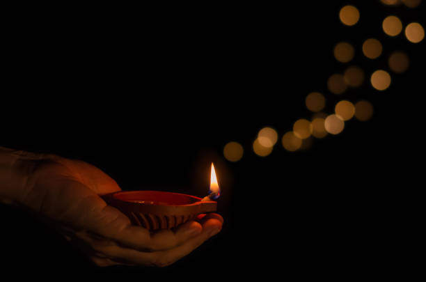 istock Hand holding the clay diya lamp lit on dark background 1414906253