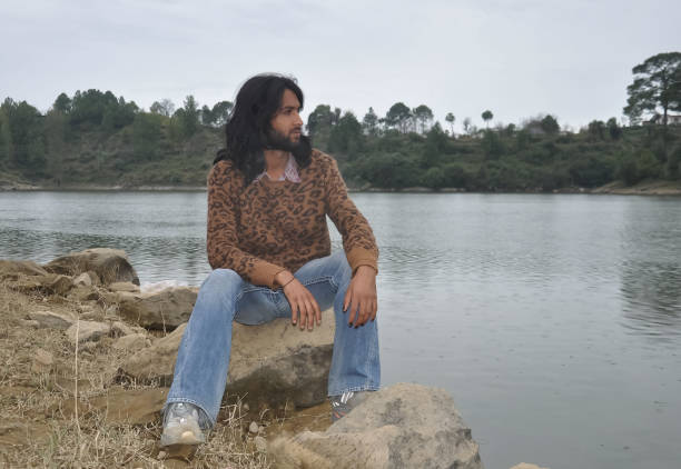 istock A good looking young man with long hair and beard looking sideways while sitting on stone by the lake 1414907864