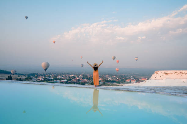 belle touriste voyageuse, une touriste regarde des montgolfières tout en faisant un signe de paix dans les piscines en travertin de pamukkale à denizli, en turquie - hierapolis photos et images de collection