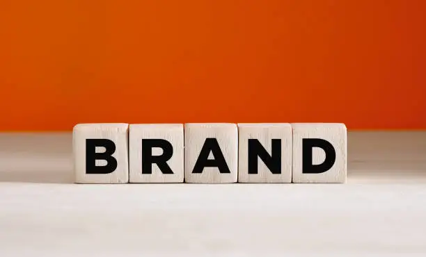 Photo of The word brand on wooden cubes on orange background with copy space. Brand identity or awareness