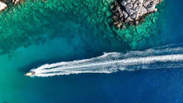 Photo of Luxury speed boat floating in open sea at summer, Yacht sailing in sea at hot summer day, Seashore of Mediterranean Sea at summer, Cruise speed boat floating in sea along rocky mountain coastline of Mediterranean Sea