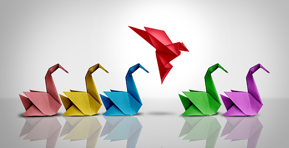 Innovative thinker concept and new idea thinking as a symbol of revolutionary innovation and inspiration metaphor as a group of paper swans and a game changer origami bird in flight.