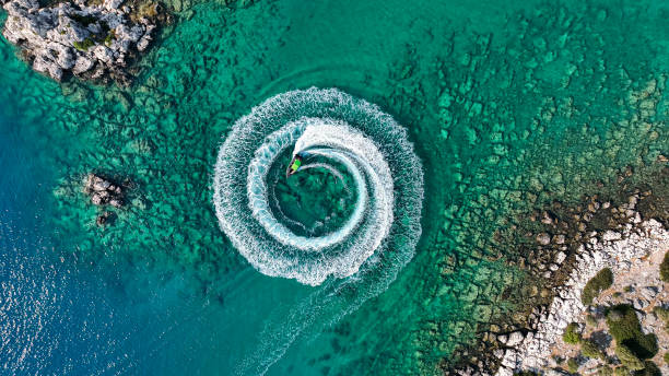 zoom arrière vue aérienne étonnante d’un homme conduisant une motomarine dans l’océan créant un motif circulaire droit vers le bas, fond d’été étonnant, couleur de l’eau et belle journée d’aventure turquoise claire sur la plage tropicale - ski boat photos et images de collection