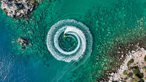 Photo of Zoom out amazing aerial view of man driving a personal watercraft in the ocean creating a straight down circular pattern,Amazing summer background, Water color and beautiful bright Clear turquoise Adventure day on tropical beach, Spinning speed boat