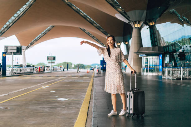 Single Woman catches taxi in airport pickup lane Young woman in casual clothing stretched out arm looking at the street to stop taxi in airport entrace kuala lumpur airport stock pictures, royalty-free photos & images
