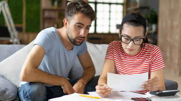 istock Young couple calculating bills at home using calculator.  Couple checking bills and documents while calculating finances sitting in the living room. Man and woman at home analyzing their finance with documents. 1414921480