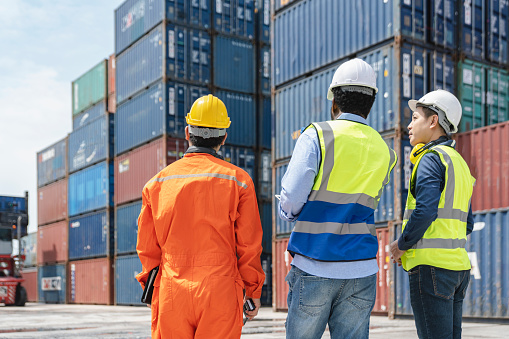 Male and female dock workers exchange work in front of port cranes