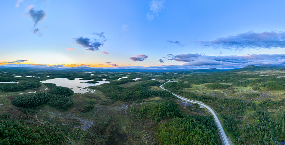 A winding road through green mountain and lake landscape in the region of Jamtland Harjedalen, Sweden. In the far back the mountain of Mittaklappen. Seen in summer.