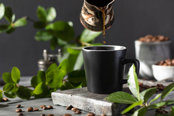 Coffee is poured into a black mug from a metal cup on a dark background.