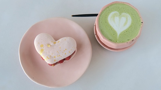 Romantic date in cafe with matcha latte and lovely heart dessert on Valentine's day, tasty sentimental gift. There is a hot drink and a heart-shaped cookie on the table. Favorite dessert in the cafe.