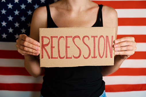 Concept of recession and financial problem in USA banking system and world economic crisis, Woman hold cardboard with word Recession against national american flag