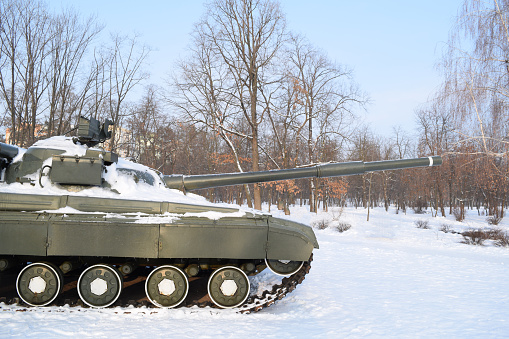 Side view of a military tank in a winter forest. Military equipment. War in winter
