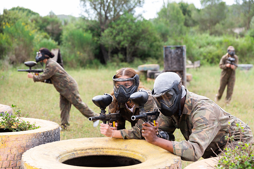 Couple of paintball players, afro american man and european woman in masks, playing paintboll outdoors