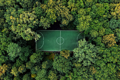 Drone top down view of beautiful shcool football field in summer deciduous forest. Calm cloudy day from tall green trees around. Empty football field, aerial shot
