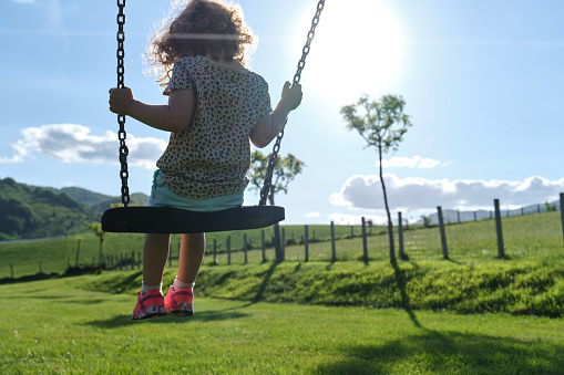 little caucasian girl alone and sad on the swing in the park - playground- concept of shyness, autism, social problems