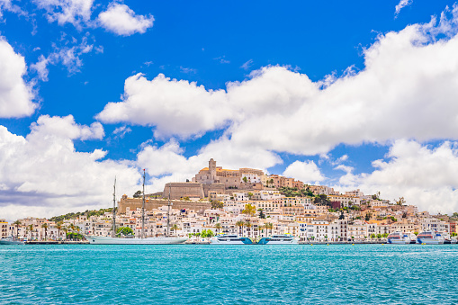 An extremely detailed wide-angle view of Eivissa's old town centre and marina. Bright sky, the warm light of a summer afternoon, picturesque clouds, turquoise waters, a moored sailing ship and fast ferries, the iconic skyline of Dalt Vila dominated by the cathedral church of Santa Maria de les Neus. Developed from RAW.