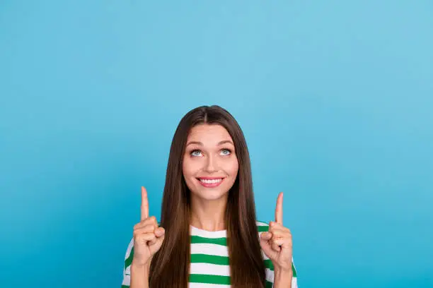 Photo of Photo of cute millennial lady indicate look up wear striped t-shirt isolated on blue color background