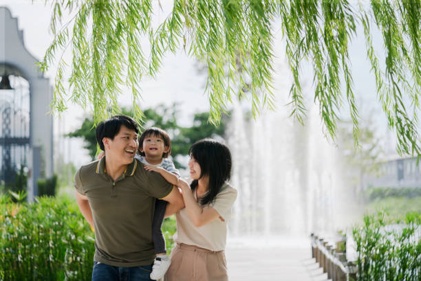 Happy Asian parents giving his little boy a piggyback ride in the park. stock photo