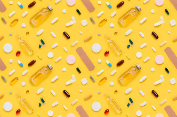 Photo of Seamless pattern of medical drugs tablets and pills assortment with ampoule glass bottle and band aid on yellow background top view
