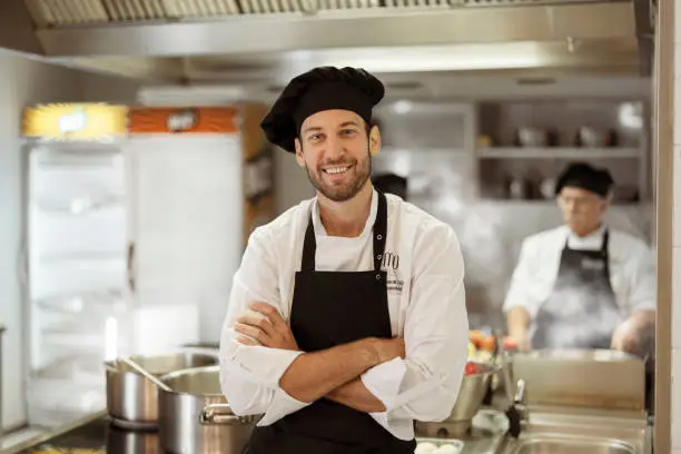 Portrait of satisfied cheerful positive chef in restaurant kitchen looking at camera