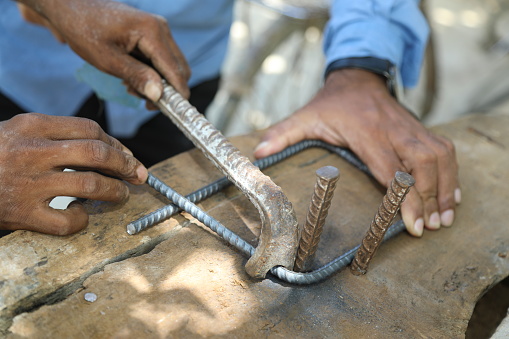 Worker bend steel rod using bender at a construction site. Closeup shot of male hand with bender bending metal rebar with manual labour. The labourer is bare handed which is unsafe for this job.