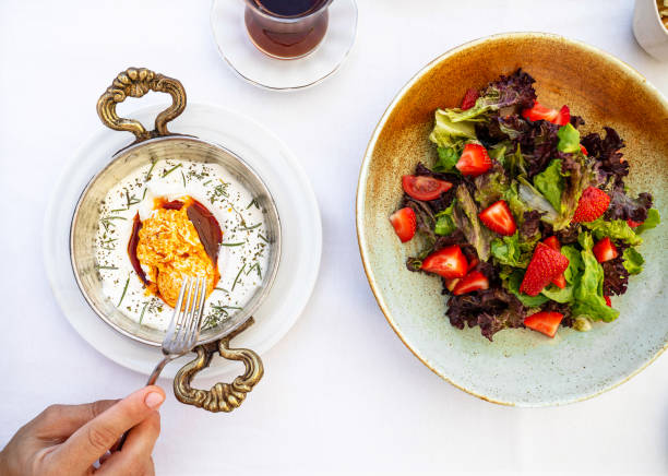 istock Turkish eggs cilbir in white bowl and fresh salad. Turkish cuisine concept. Poached eggs with yogurt and spicy butter sauce. 1414933760