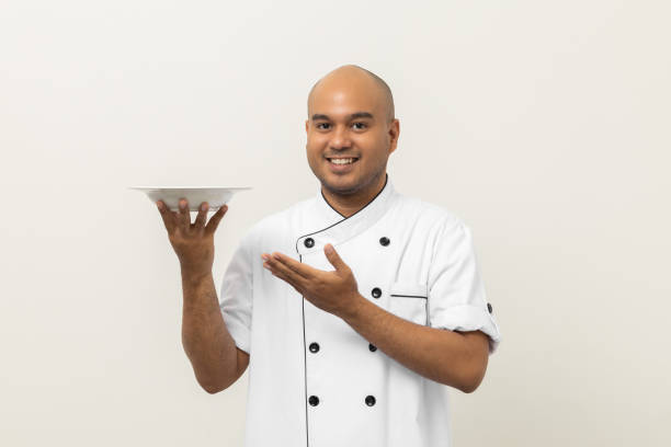 istock Smiling Young handsome asian man chef in uniform holding empty plate delicious dish menu good taste on isolated. Cooking indian man Occupation chef or baker People in kitchen restaurant and hotel. 1414934236