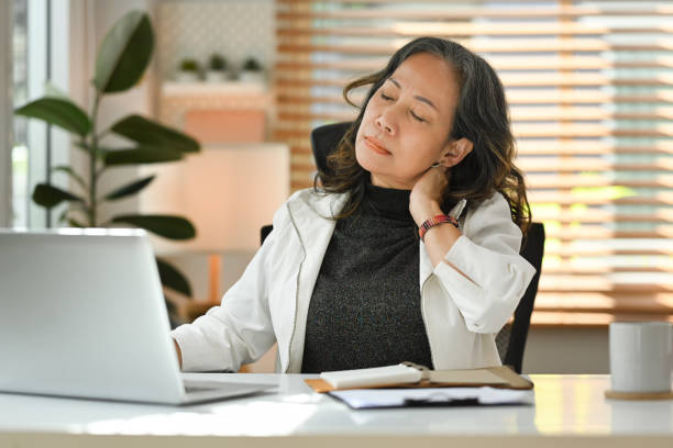 mujer de negocios de mediana edad frotándose el cuello, sufriendo de dolor de cuello durante el lugar de trabajo en casa. - pain pressure fotografías e imágenes de stock