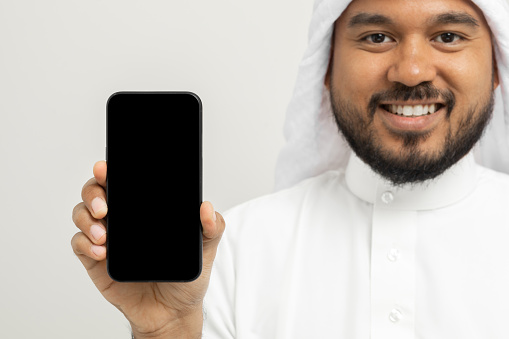 Portrait of arabic man with kandura dress using cellphone on isolated white background. Arab business people holding smartphone.