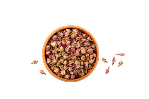 Dried flowers, whole rose buds in ceramic bowl on white background. Pink Rose buds used in herbal medicine, perfumery and culinary. Selective focus, copy space.