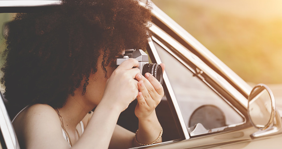 Tourist, travel and photographer using camera to take photos while on an adventure, road trip and sightseeing while traveling with a car. Closeup of afro woman enjoying sights while on solo journey