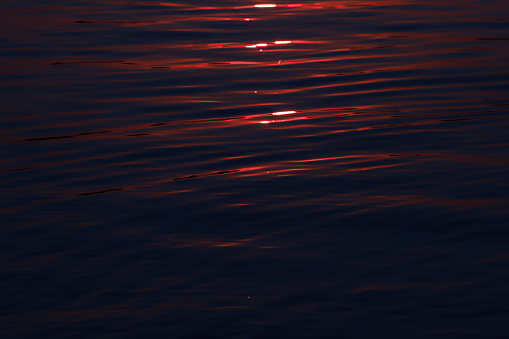 Dark blue waves with red sun glare on a summer evening at a pink sunset, close up. River, lake or sea surface background
