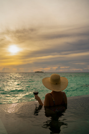 Rear view of a woman looking ocean from infinity pool at sunset