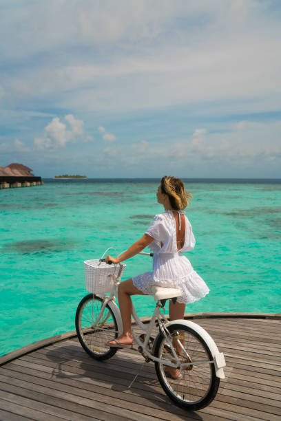 Beautiful woman posing with bicycle on wooden jetty in Maldives stock photo