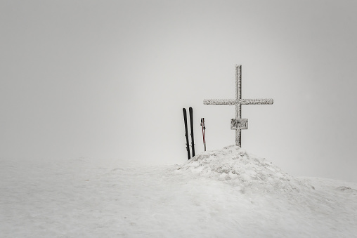 Frozen snowy cross with ski in the fog on the winter mountain top