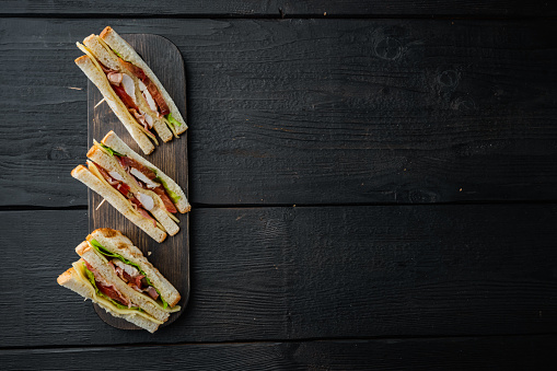 Homemade turkey club sandwich, on black wooden background, top view with copy space for text