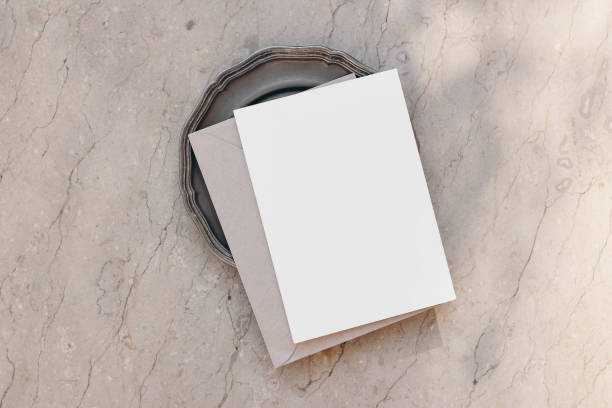 istock Summer stationery still life. Modern minimal composition. Greeting card, invitation mock up scene with craft envelope and vintage silver plate in sunlight. Beige textured marble background. Flat lay, 1414945378