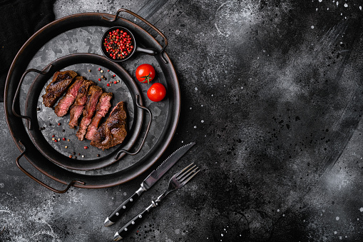 Medium grilled steak, on black dark stone table background, top view flat lay, with copy space for text.