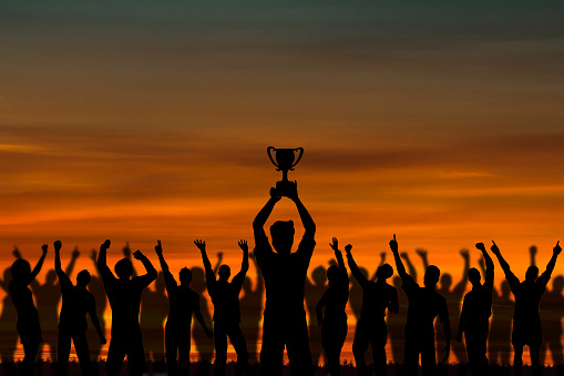 Silhouette of man raising trophy with crowd people. Success, freedom, friendship and unity concept.