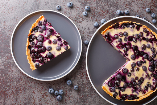 Homemade fresh blueberry tart with custard close-up in a plate on the table. Horizontal top view from above