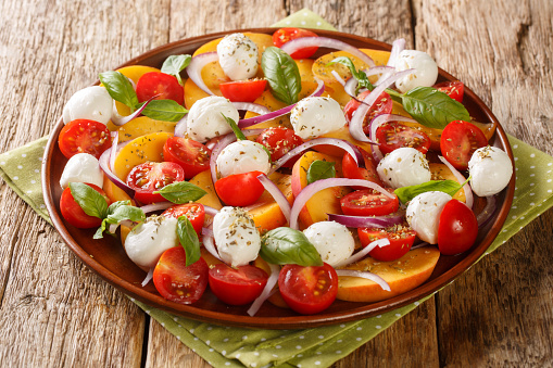 Caprese Salad with peaches, mozzarella cheese, cherry tomatoes, onions and basil close-up in a plate on a wooden table. Horizontal