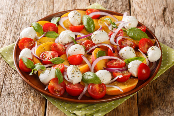 Caprese Salad with peaches, mozzarella cheese, cherry tomatoes, onions and basil close-up in a plate. Horizontal stock photo