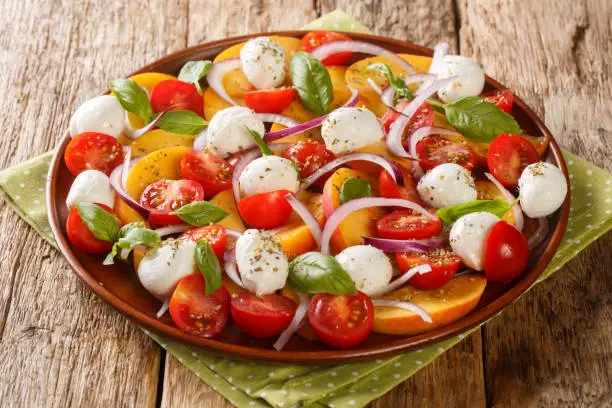 Photo of Caprese Salad with peaches, mozzarella cheese, cherry tomatoes, onions and basil close-up in a plate. Horizontal