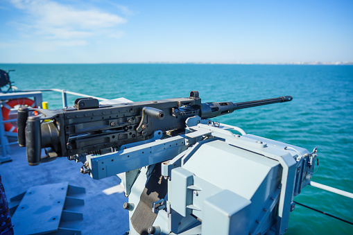 Color image of an automated machine gun on the deck of a military ship, at sea.
