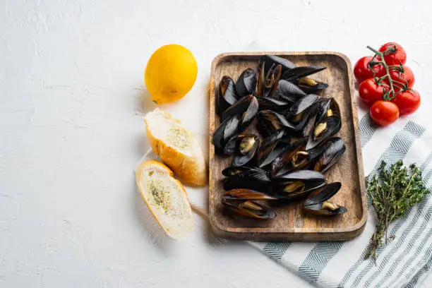 Photo of Raw Mussels with herbs lemon and baguette, on wooden tray, on white background , with copyspace  and space for text