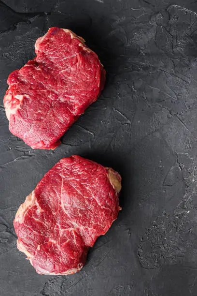 Raw rump steaks from organic beef meat cuts over black textured  background, top view with space for text