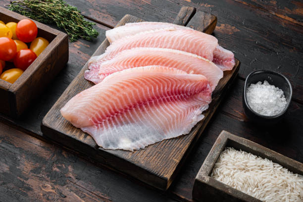 古い木製のテーブルの上にバスマティライスとチェリートマトの材料と白身魚のフィレ - prepared fish tilapia fillet seafood ストックフォトと画像