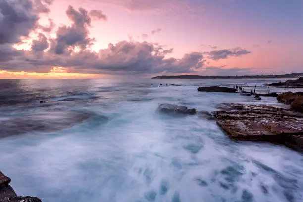 Beautiful dawn sky overlooking ocean and rock pool used by swimmers