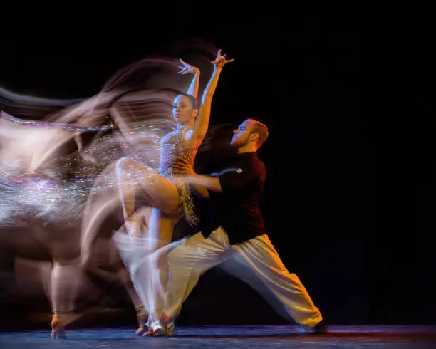 Photo of Flight of feelings. Two professional dancers dancing ballroom dance isolated on dark background with mixed light. Concept of art, beauty, fashion